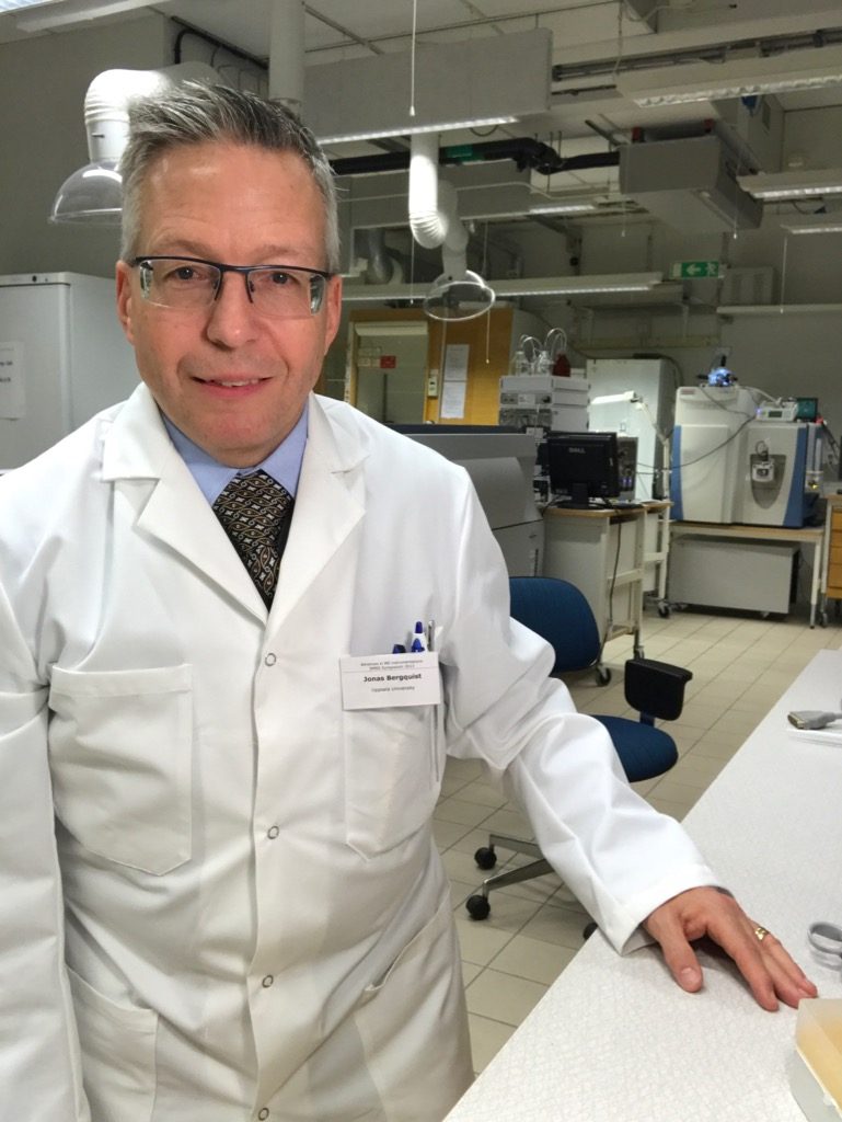 Picture of Jonas Bergquist in the lab. He has a warm smile and is wearing a white lab coat with his name tag on it.