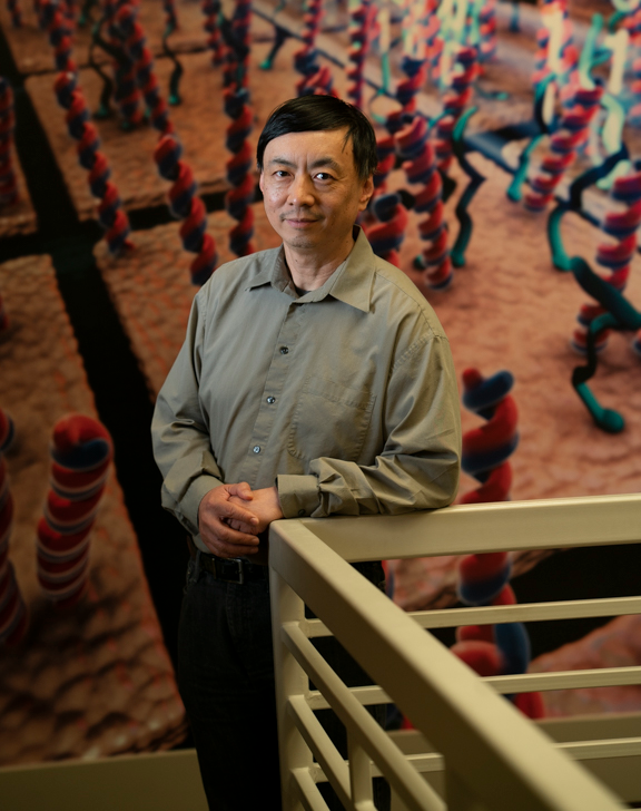 Dr. Wenzhong Xiao standing in front of a colorful, science-themed background.