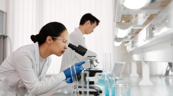 Woman researcher looking through microscope. Male in background