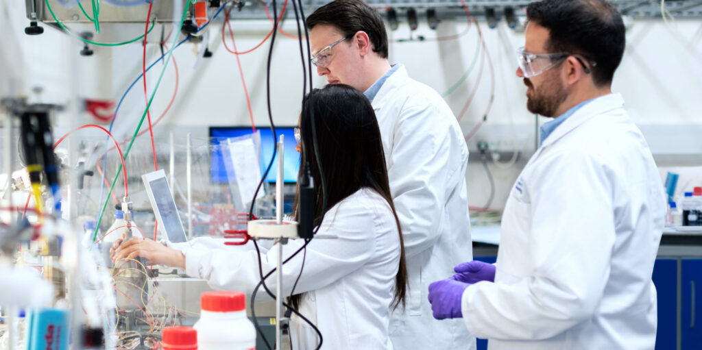 One woman researcher and two male researchers facing left in lab