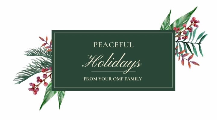 The image features a holiday greeting card with a dark green background. In the center, it reads "Peaceful Holidays from your OMF Family!" in elegant, light-colored script. Surrounding the text are watercolor illustrations of festive greenery and berries on both sides.