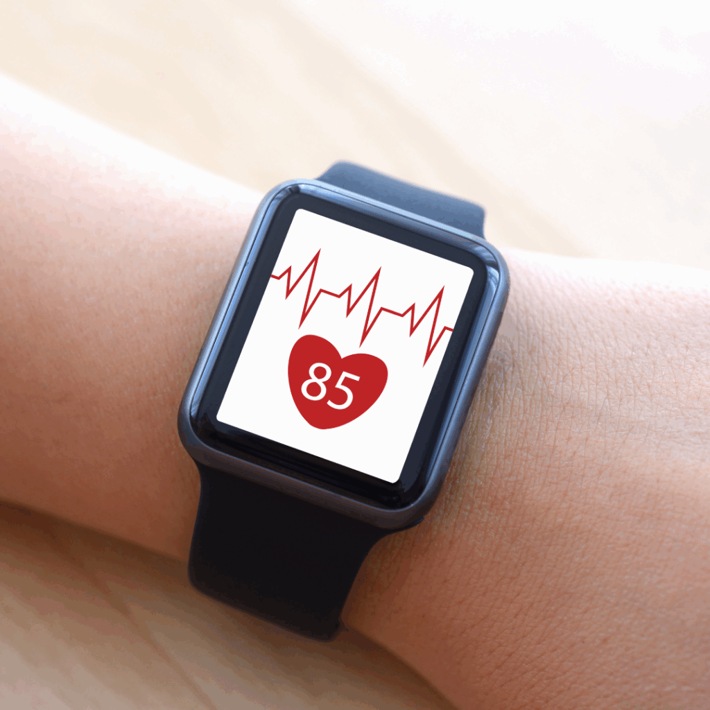 This image shows a close-up of a smartwatch on someone's wrist. The screen displays a heart rate monitor with a red heart icon showing the number 85, representing the person's current heart rate in beats per minute (BPM).
