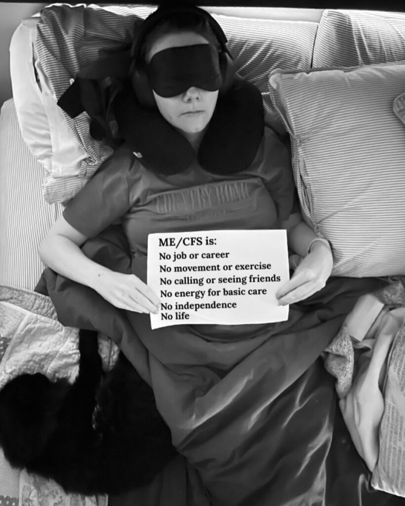 Lysh is holding a sign that reads: “ME.CFS is: No job or career, No movement or exercise, No calling or seeing friends, No energy for basic care, No independence, No life.