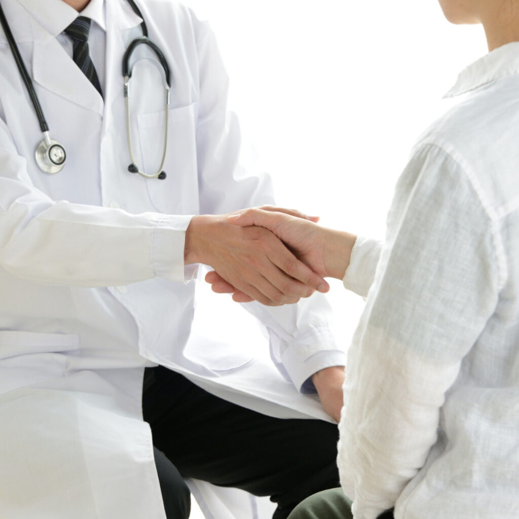A researcher in a white coat with a stethoscope shakes hands with a research participant.